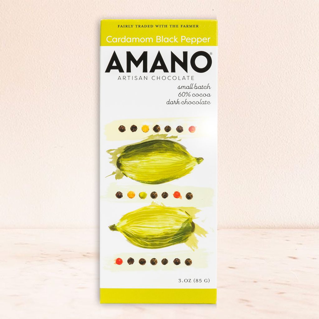 Amano artisan chocolate bar featuring cardamom and black pepper is set against a light background. The packaging showcases artistic green cardamom illustrations.
