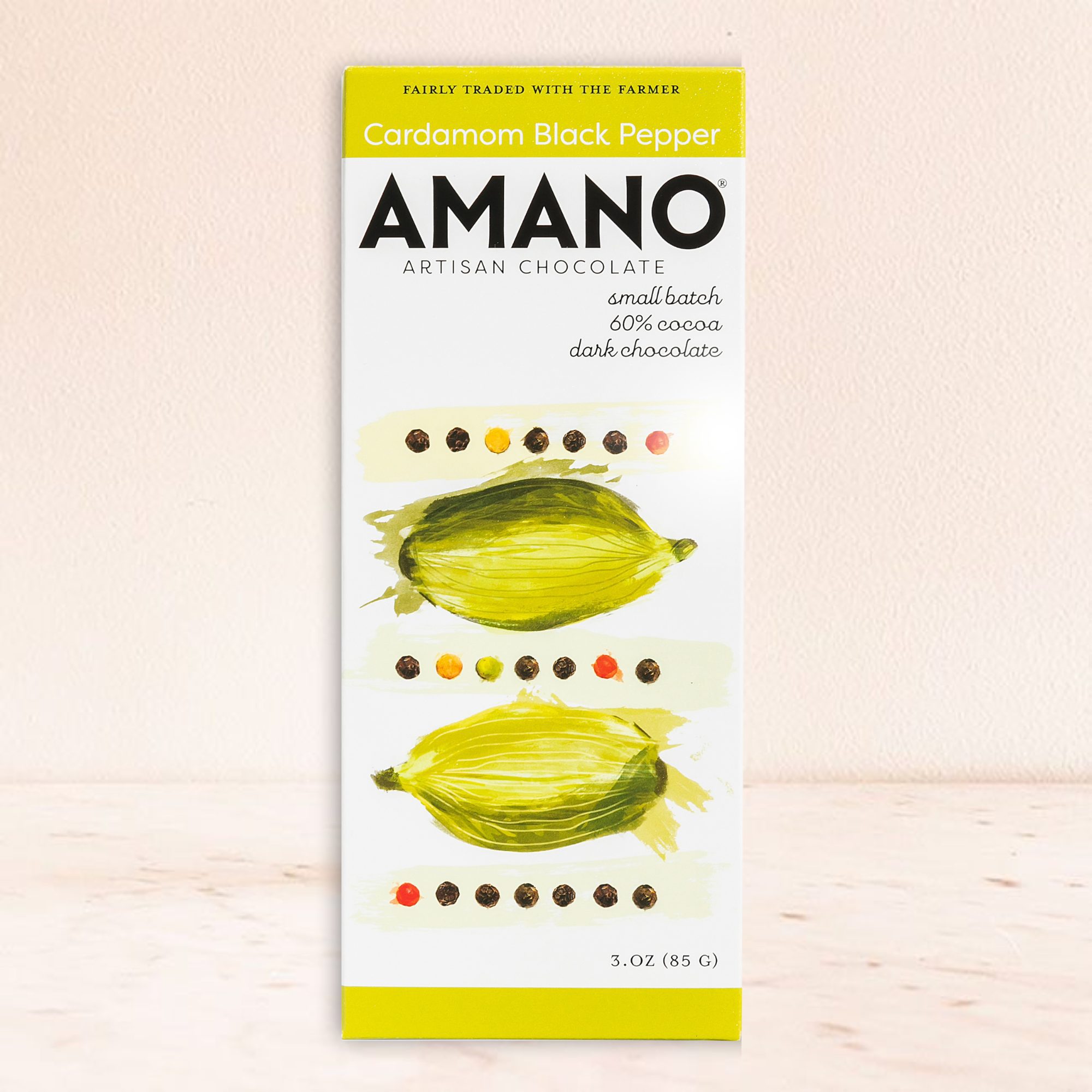Amano artisan chocolate bar featuring cardamom and black pepper is set against a light background. The packaging showcases artistic green cardamom illustrations.