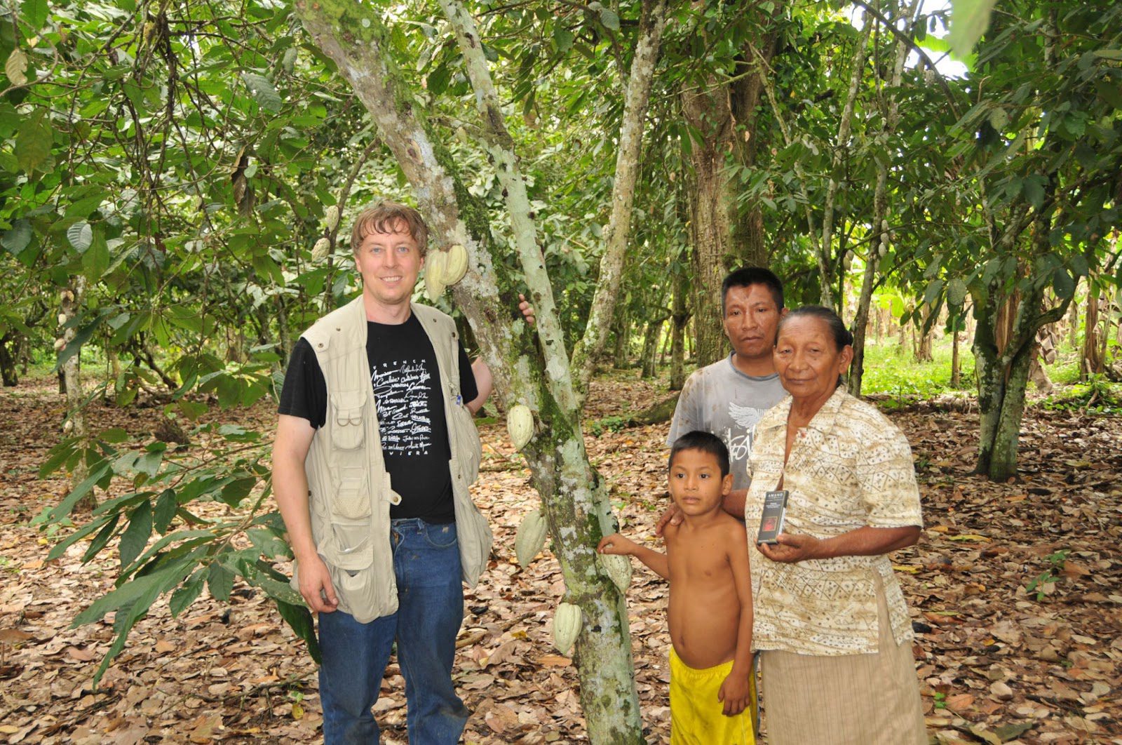 A man and two children stand together beside a large tree in a sunny outdoor setting.