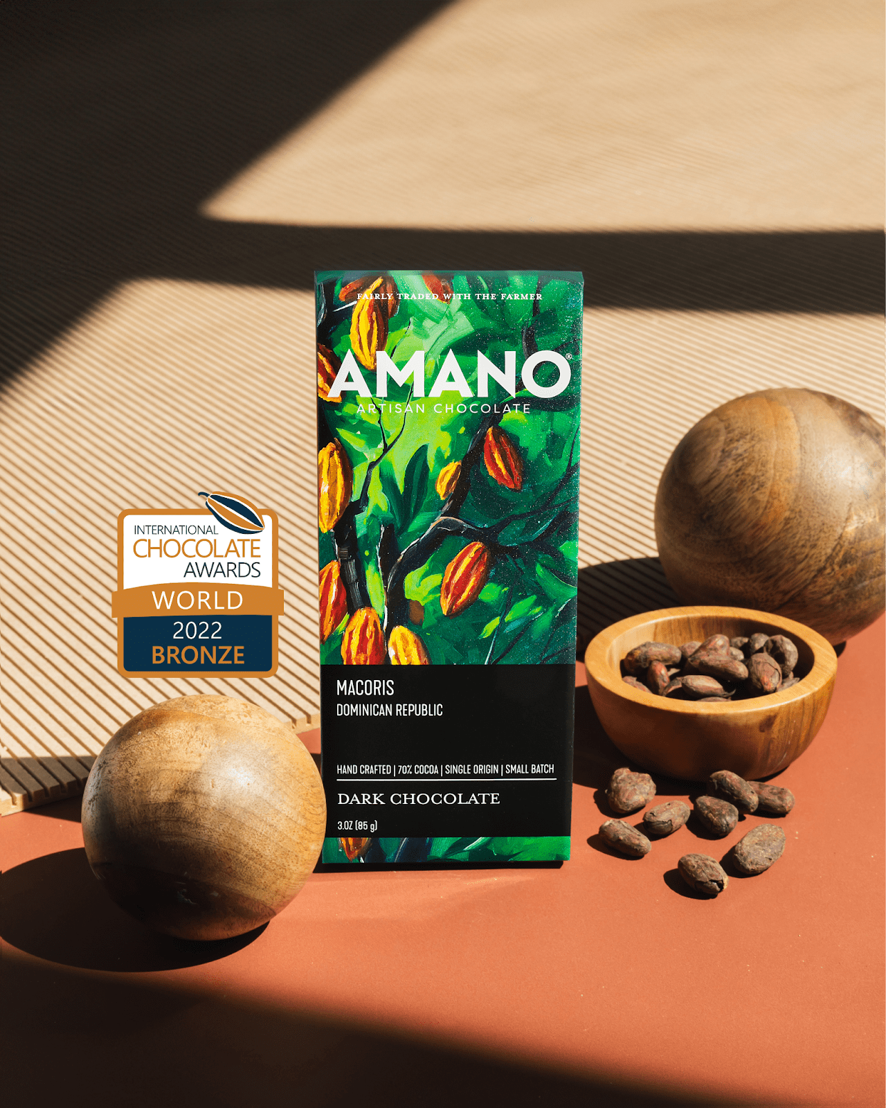 Amano Artisan Chocolate bar with a 2022 International Chocolate Awards Bronze medal, displayed with cocoa beans and wooden spheres.