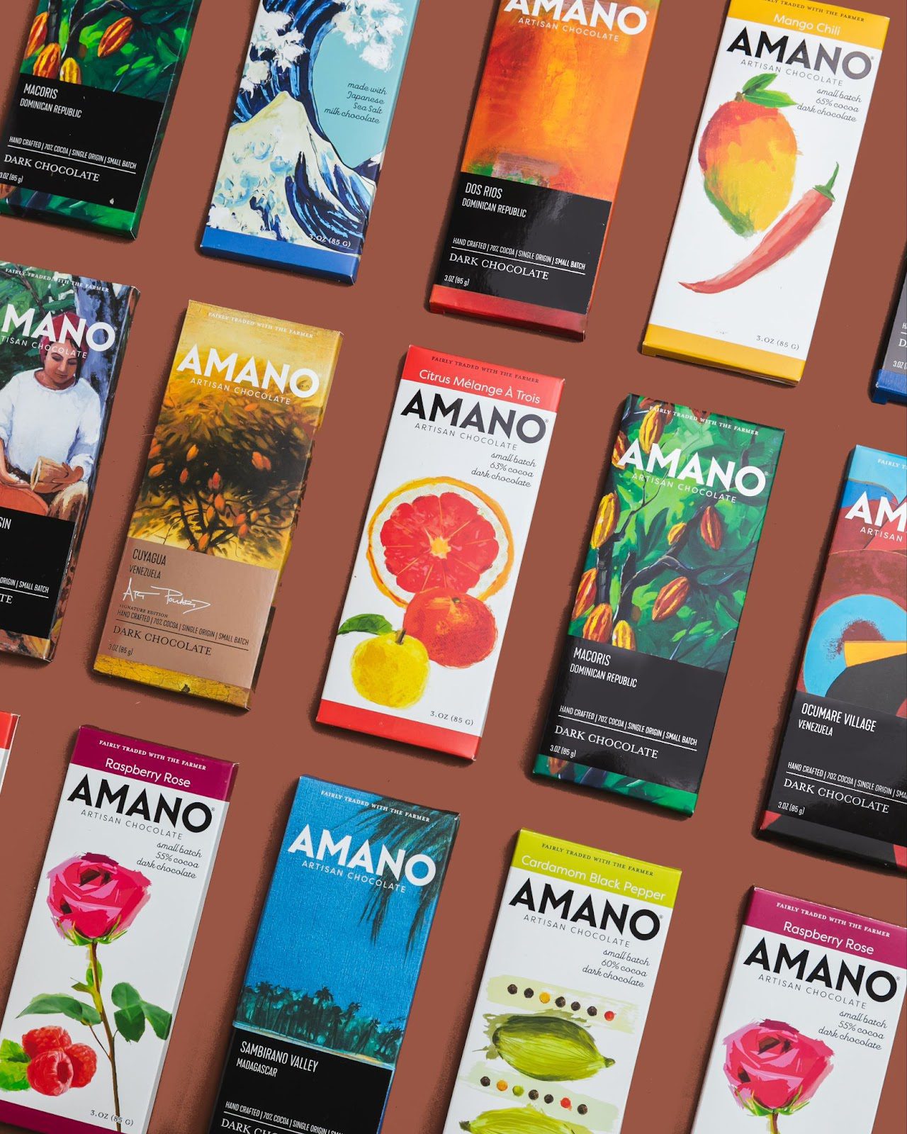 Assorted Amano Artisan Chocolate bars with colorful packaging on a brown surface.