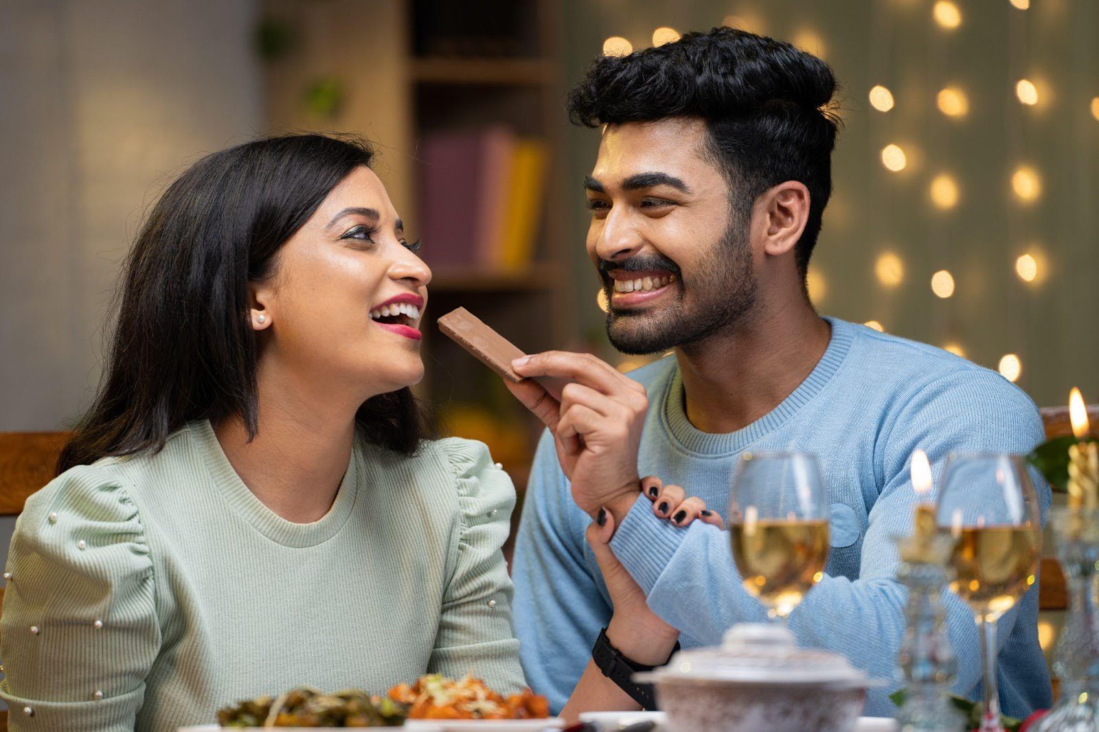 A man and woman share chocolate at a dinner table enjoying a moment together in a cozy setting