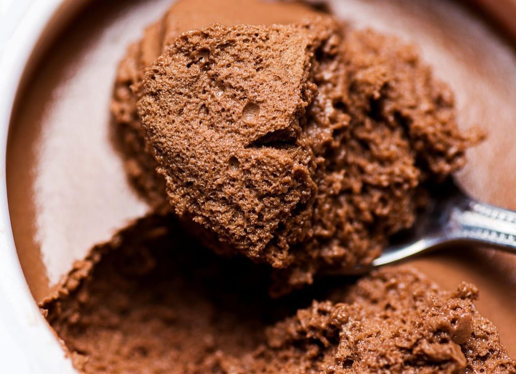 A bowl of rich chocolate ice cream with a silver spoon resting beside it