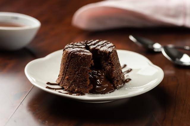 A creamy chocolate pudding served on a white plate next to a cup of hot tea