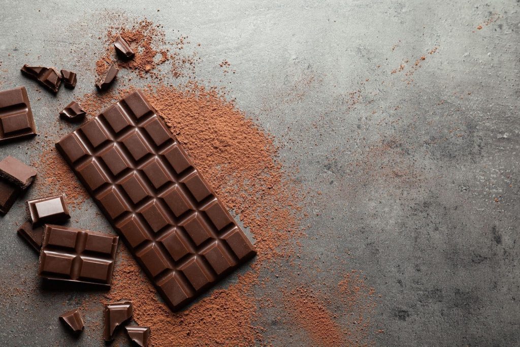 A rich chocolate bar with broken pieces lies on a textured gray surface