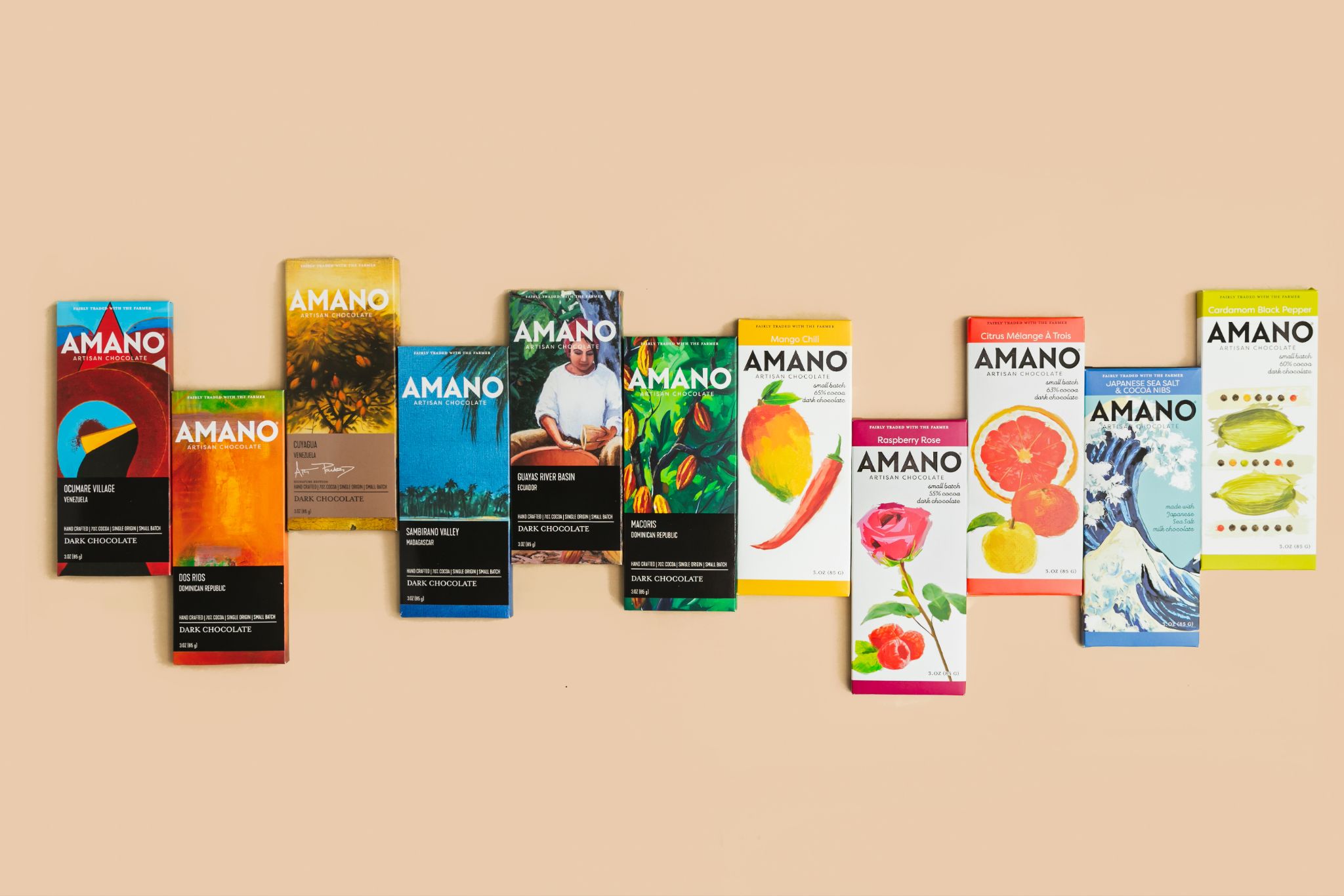 A row of various brightly colored Amano Artisan Chocolate bars arranged neatly against a plain beige background.