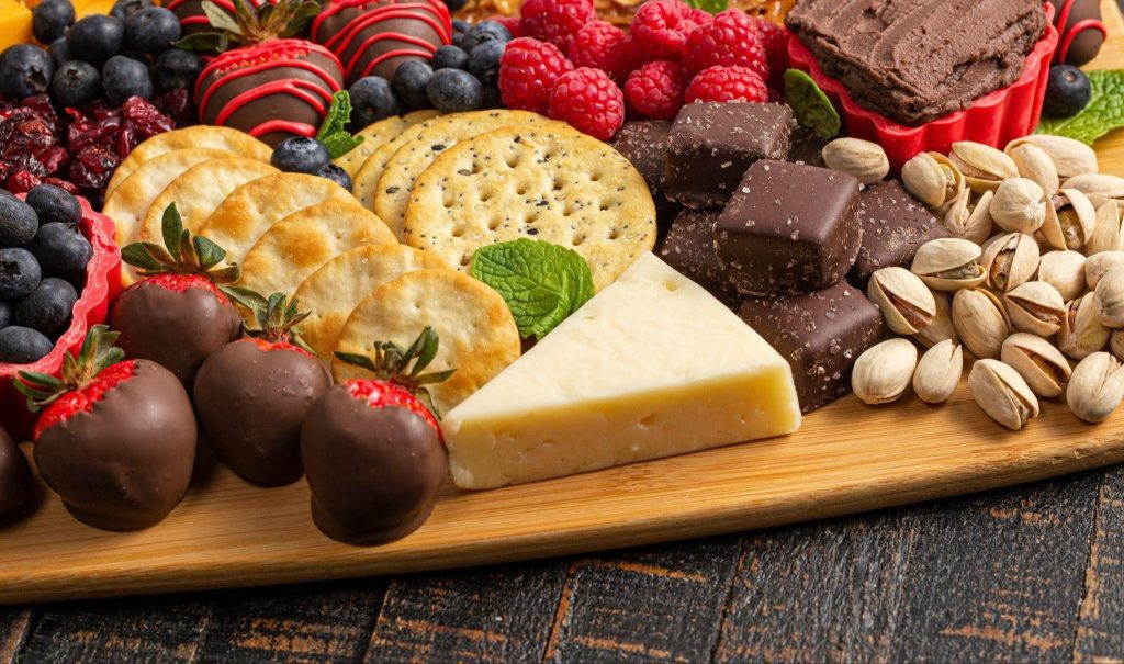 A wooden platter displaying a variety of fresh fruits and pieces of chocolate arranged artfully