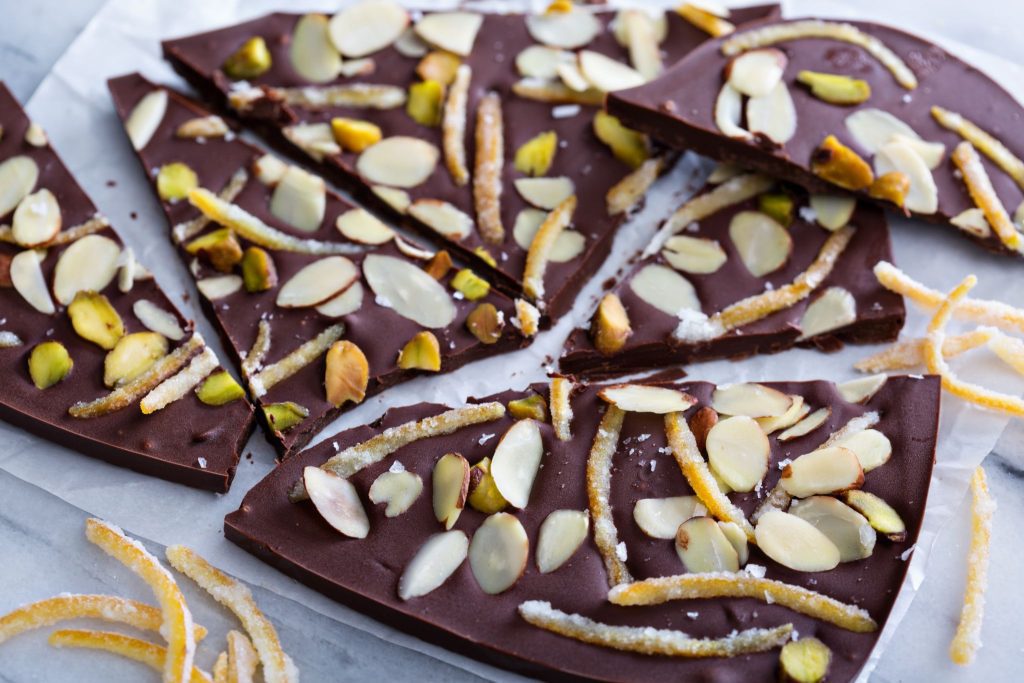 Broken pieces of dark chocolate bark topped with sliced almonds, pistachios, and candied orange peel.