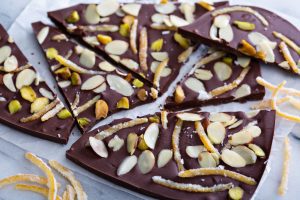 Broken pieces of dark chocolate bark topped with sliced almonds, pistachios, and candied orange peel.