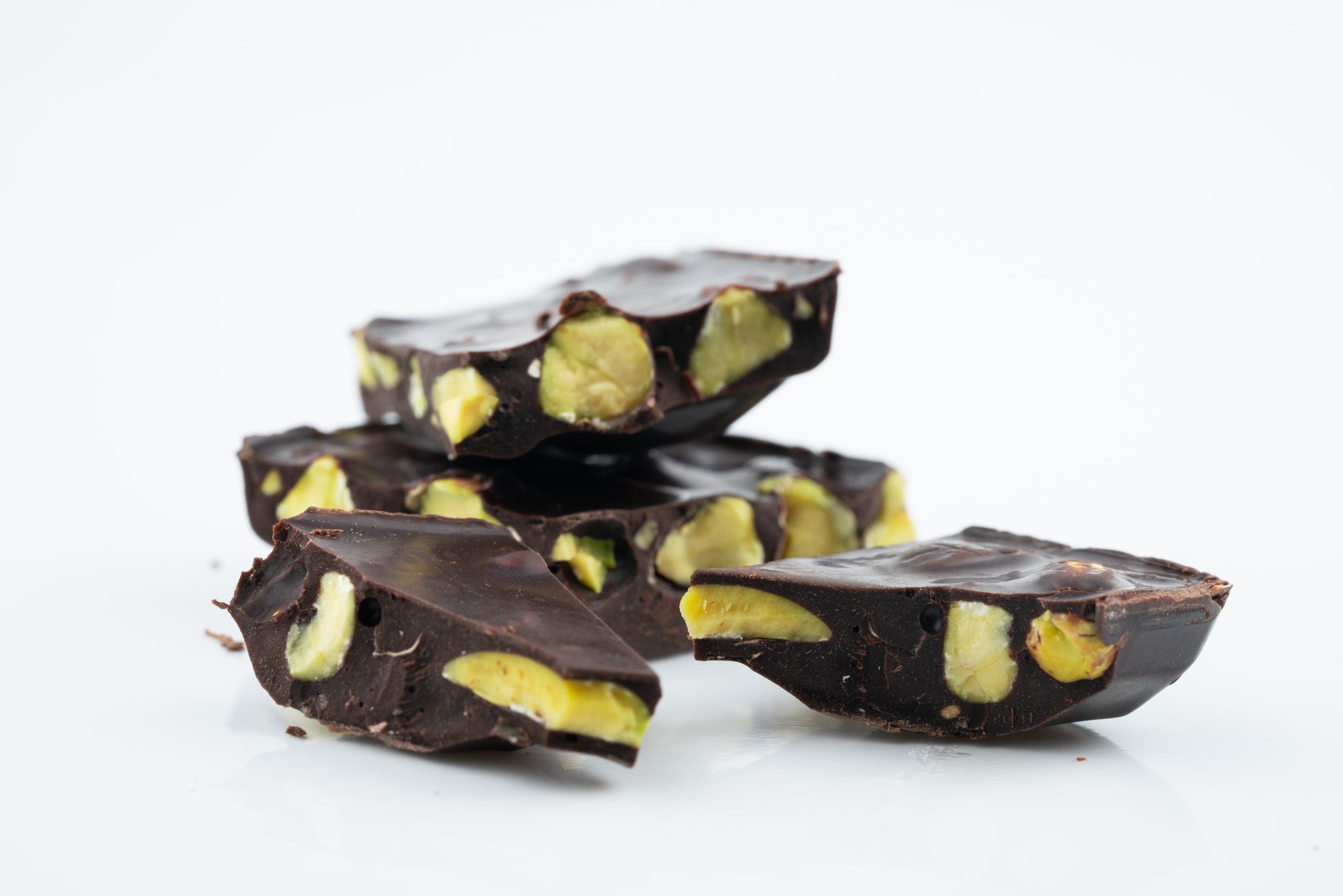 Stacked pieces of thick dark chocolate bark filled with whole pistachios against a plain white background.