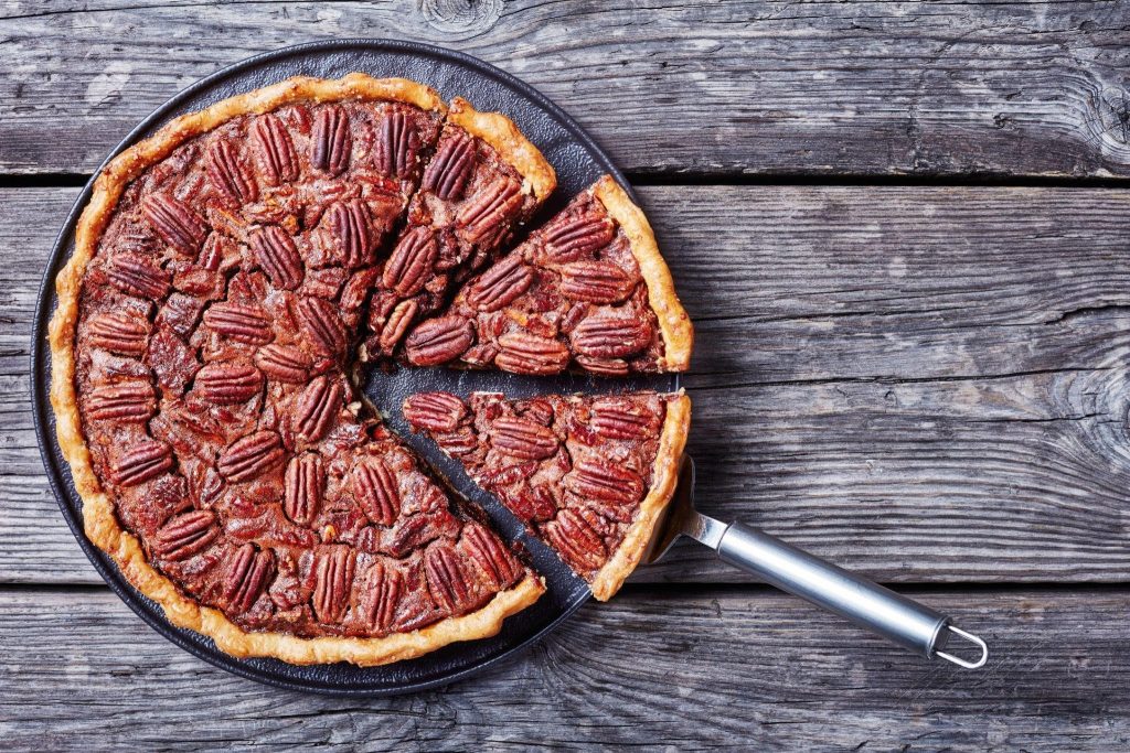 A freshly baked pecan pie sits on a rustic wooden table showcasing its golden crust and rich filling.