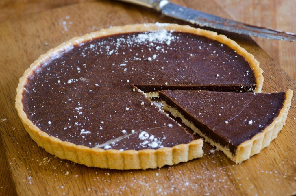 A partially eaten chocolate tart revealing its smooth filling and textured crust